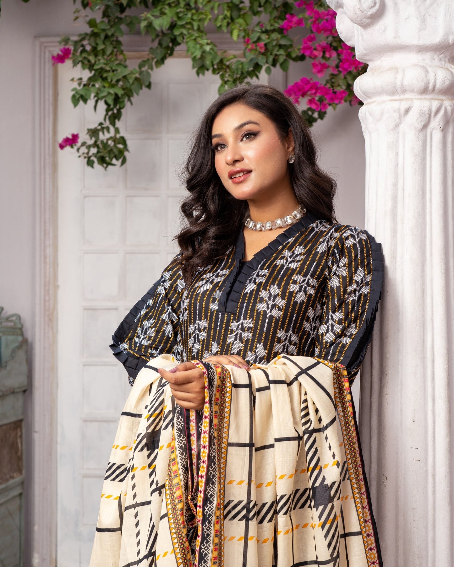 A woman standing with one hand against a backdrop of a traditional Indian building, wearing a digital printed lawn fabric with a geometric pattern in beige and other colors.
